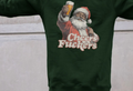 A person wearing a dark green sweatshirt featuring a vintage-style Santa holding a beer and the text "Cheers Fu**ers," conveying humor and festive irreverence.
