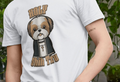 A person wearing a white Dog T-shirt with a cartoon of a Shih Tzu dressed as a priest, featuring a cross necklace and the words "Holy Shih Tzu." The background has green plants, creating a playful and humorous tone.