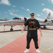 A mountain of a man stands confidently on a red carpet in front of a private jet. He's wearing sunglasses, a black