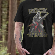 A person stands in a forest, wearing a black t-shirt featuring an illustration of a sci-fi character playing a red electric guitar, with the words
