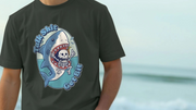 Person wearing a dark funny animal t-shirt featuring a cartoon shark biting a skeleton with the text