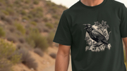 A person wears a dark green funny graphic t-shirt with a detailed crow illustration perched on branches, with the witty slogan