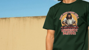 A person wearing a dark green funny T-shirt with a graphic of Jesus as a DJ and the words