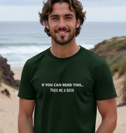 Smiling man on a beach wearing a dark green T-shirt with the joke text,
