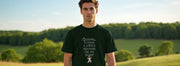 A man stands outdoors wearing a dark funny shirt with text,