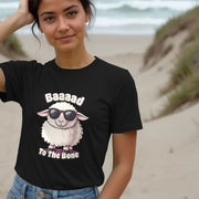 Smiling woman on a beach wearing a black Women's t-shirt with a cartoon sheep in sunglasses. Text reads,