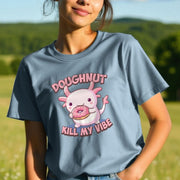 A woman in a blue Kawaii T-shirt stands in a sunny field. The shirt features a cute axolotl holding a doughnut, with the text