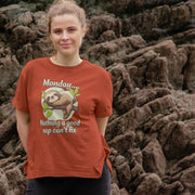 A Woman stands outdoors against a rocky background, wearing a rust-colored Women's Animal T-Shirt with a sloth graphic and text saying,