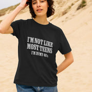 A woman stands on a sandy beach, wearing a black birthday T-shirt with white text that reads,