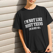 A Woman stands against a light-colored, textured wall wearing a black Slogan T-shirt with bold white text: