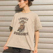 Young Woman wearing a beige Rude Women's T-shirt showing a cartoon bull sitting on a toilet, with the text 