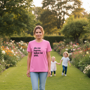 Woman wearing a pink t-shirt with the slogan 'do no harm take no shit' in a garden with two children.